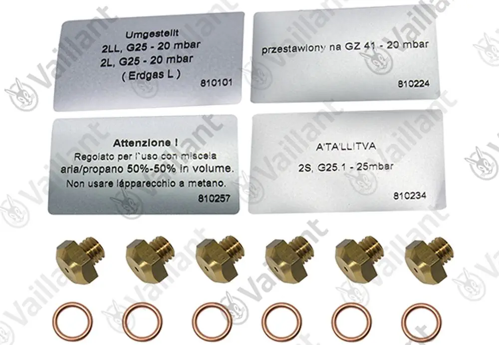 Düsenwechselsatz von Vaillant mit mehreren Düsen und Kupferdichtungen, Anleitungshinweisen in verschiedenen Sprachen auf Metalltafeln.